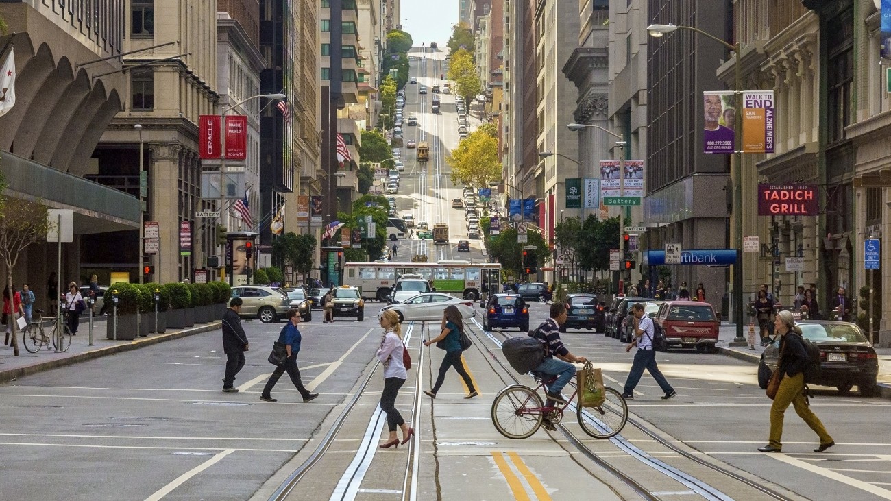 A photo of people walking and biking on Market Street, with a bus and cars in the background