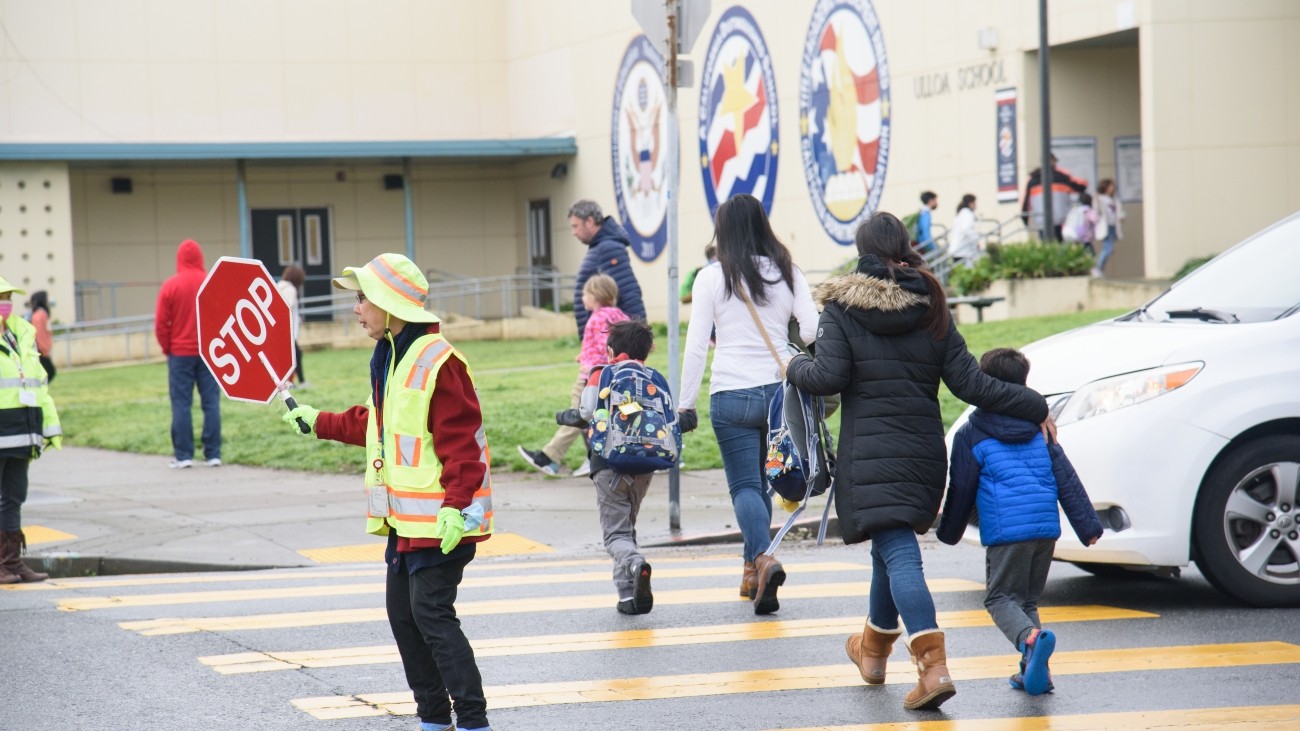 Crossing guard holding stop sign with adults and children crossing in crosswalk