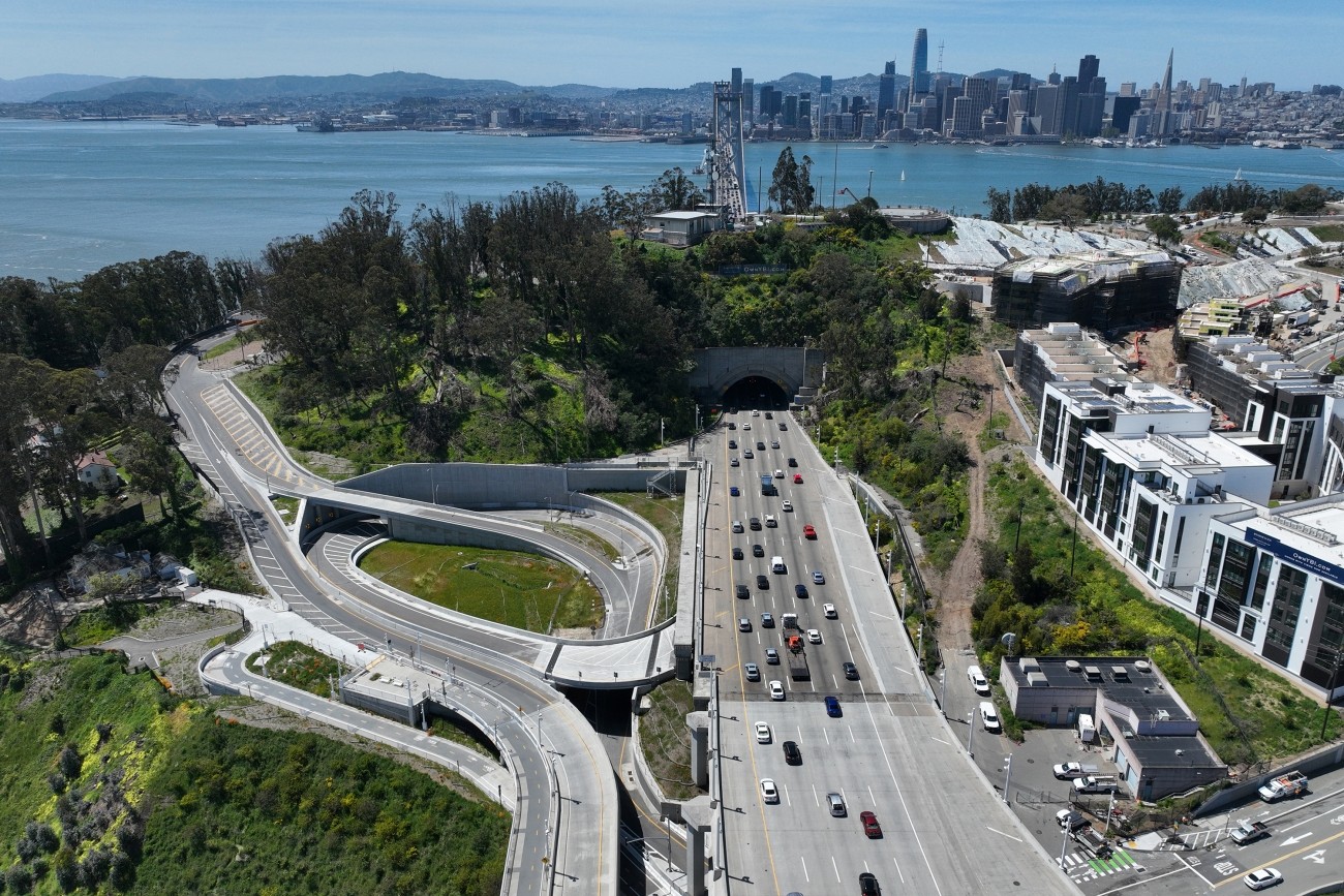 An aerial view of the completed Southgate Road project on Yerba Buena Island. The west span of the Bay Bridge and San Francisco skyline stand in the background.