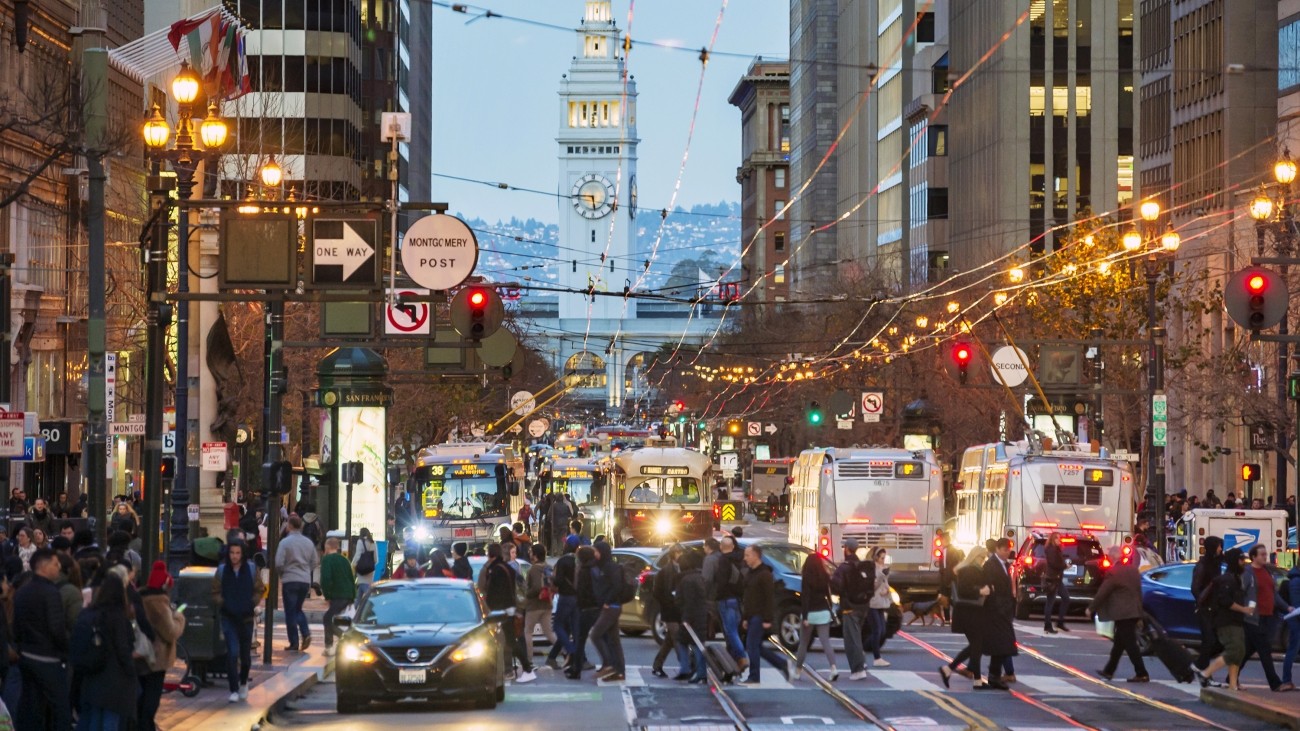 An image of buses and people walking on Market Street in the early evening