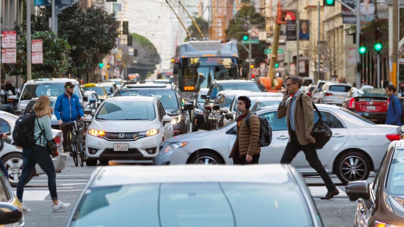 People cross crowded Mission Street as a bus waits in traffic