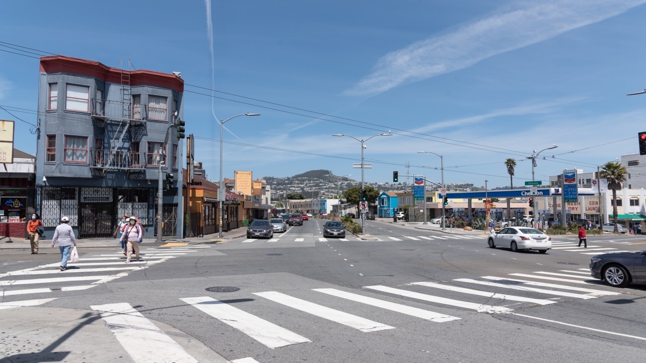 View of the Mission Street and Geneva Avenue intersection with cars and pedestrians.