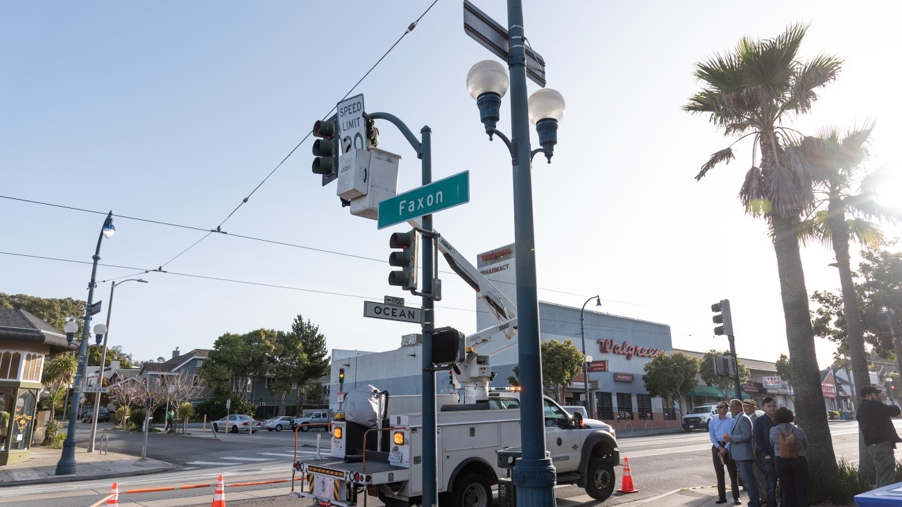 Worker installing a 20 mph sign on traffic post at Faxon and Ocean