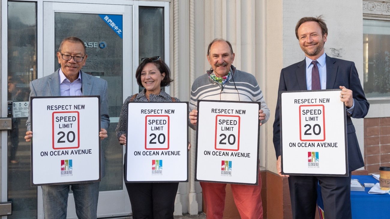 Transportation officials and community advocates holding signs that read "respect new 20 mph speed limit on Ocean Avenue"