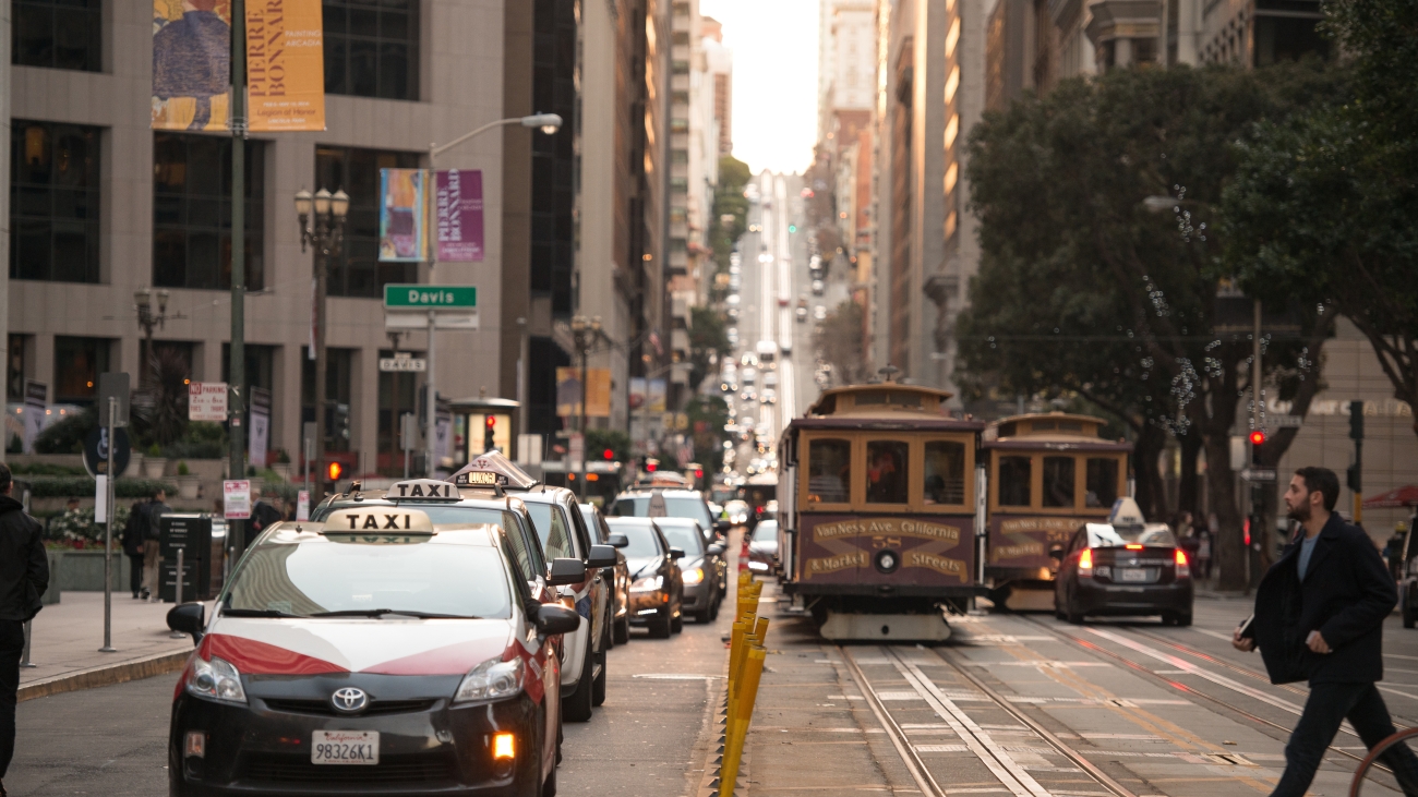 Taxis, vehicles, and cable cars on road with a pedestrian crossing in intersection