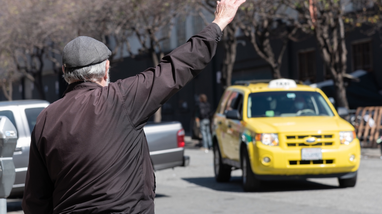 Person with hat raising arm to hail yellow tax cab 