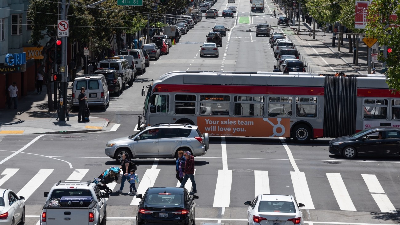 Muni buses, vehicles, and pedestrians on road along 4th Street