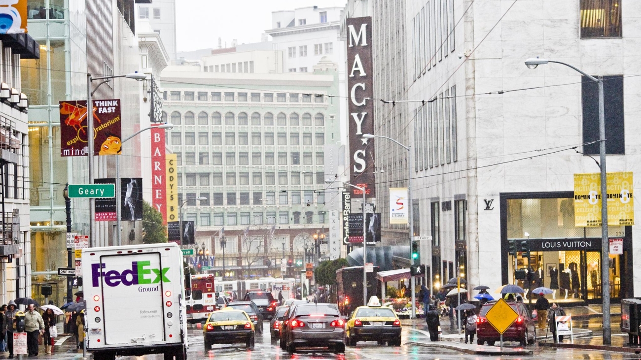 Vehicles and a Fedex truck along Stockton and Geary Streets. Market Street and Macy's signage visible in the distance. 