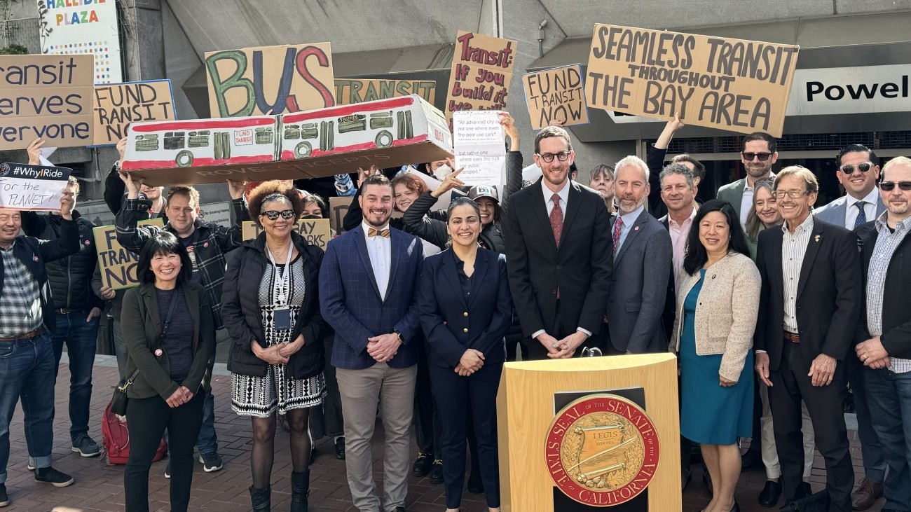 Group of transportation officials and stakeholders standing in front of Powell Station, some holding signs to support transit