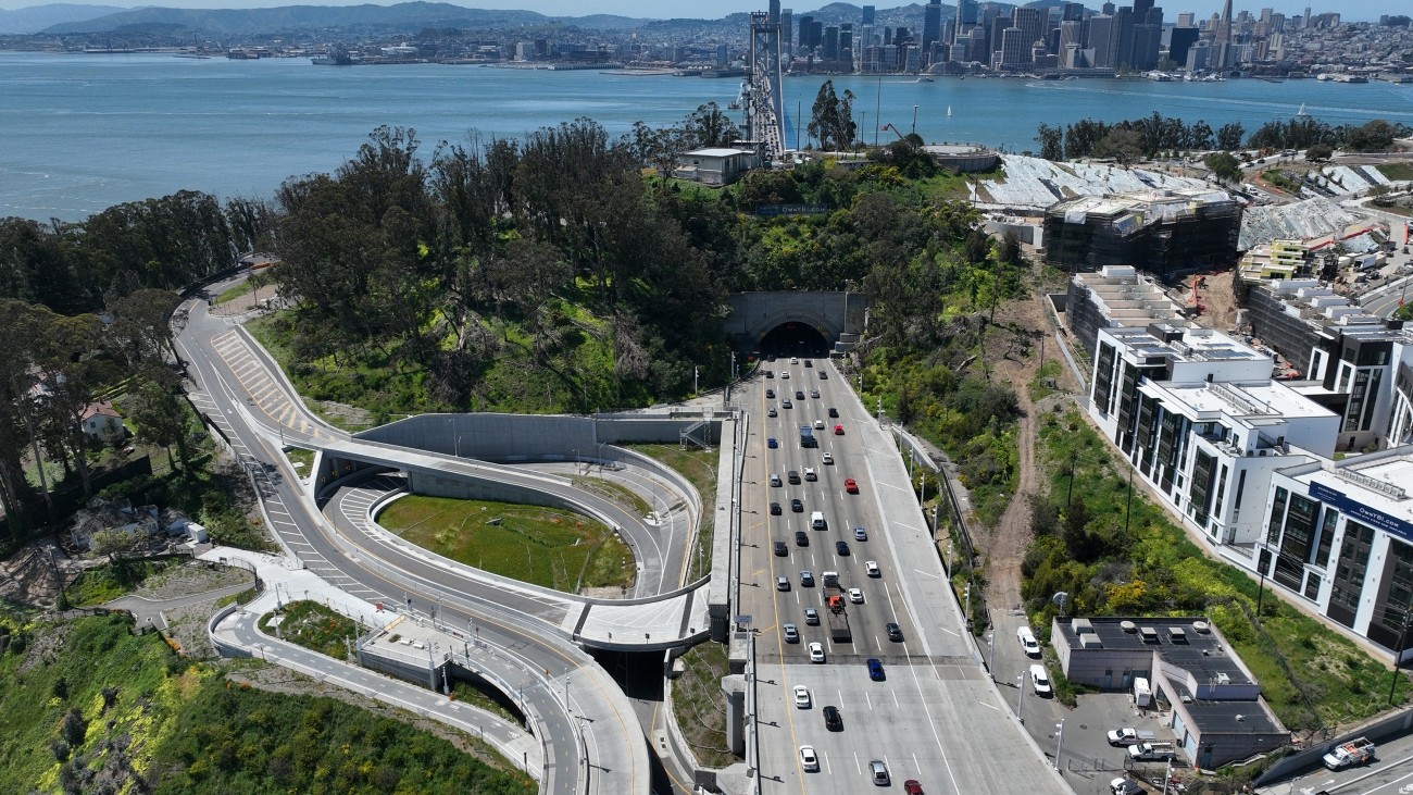 An aerial view of the completed Southgate Road project on Yerba Buena Island. The west span of the Bay Bridge and San Francisco skyline stand in the background.