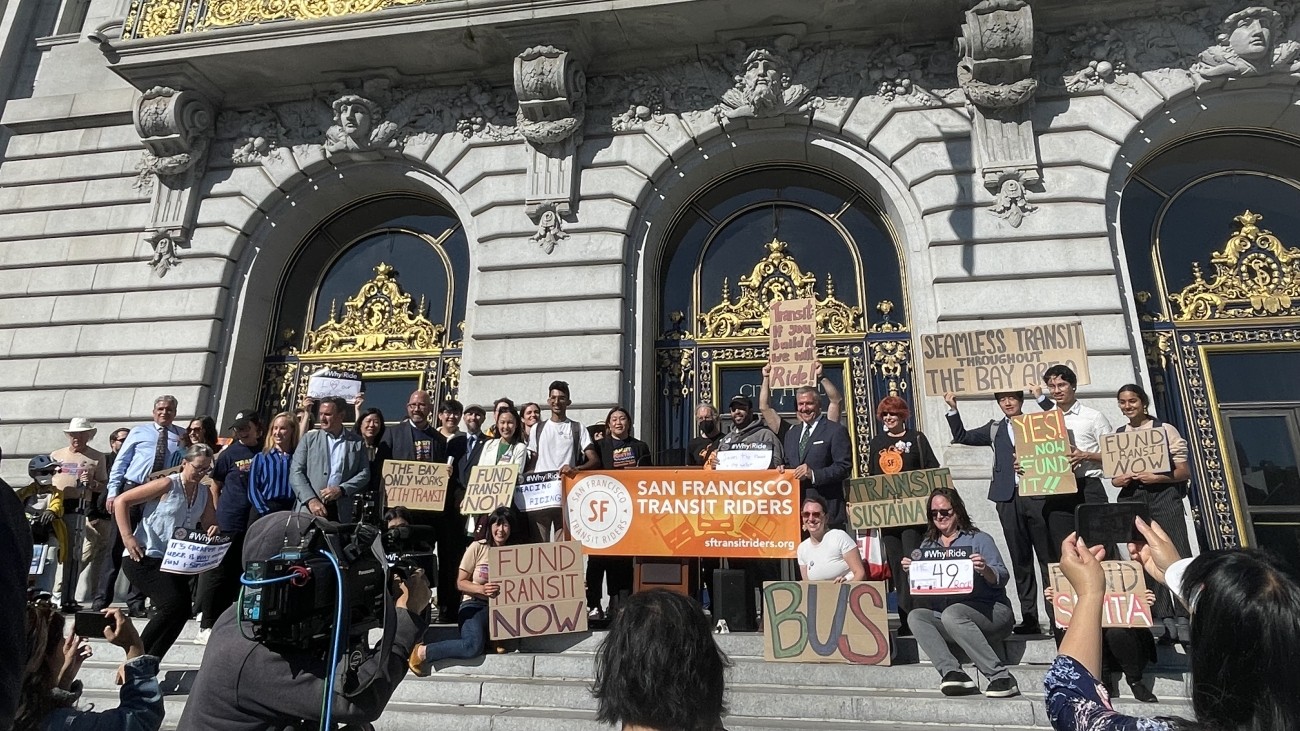 Local city and transportation officials, community advocates and leaders gathered in front of City Hall holding signsand 