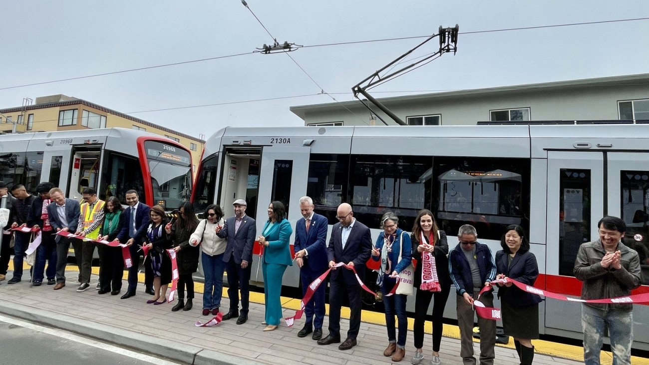 City officials, transportation officials and staff, and community members gathered in front of an L Taraval train to cut a ribbon