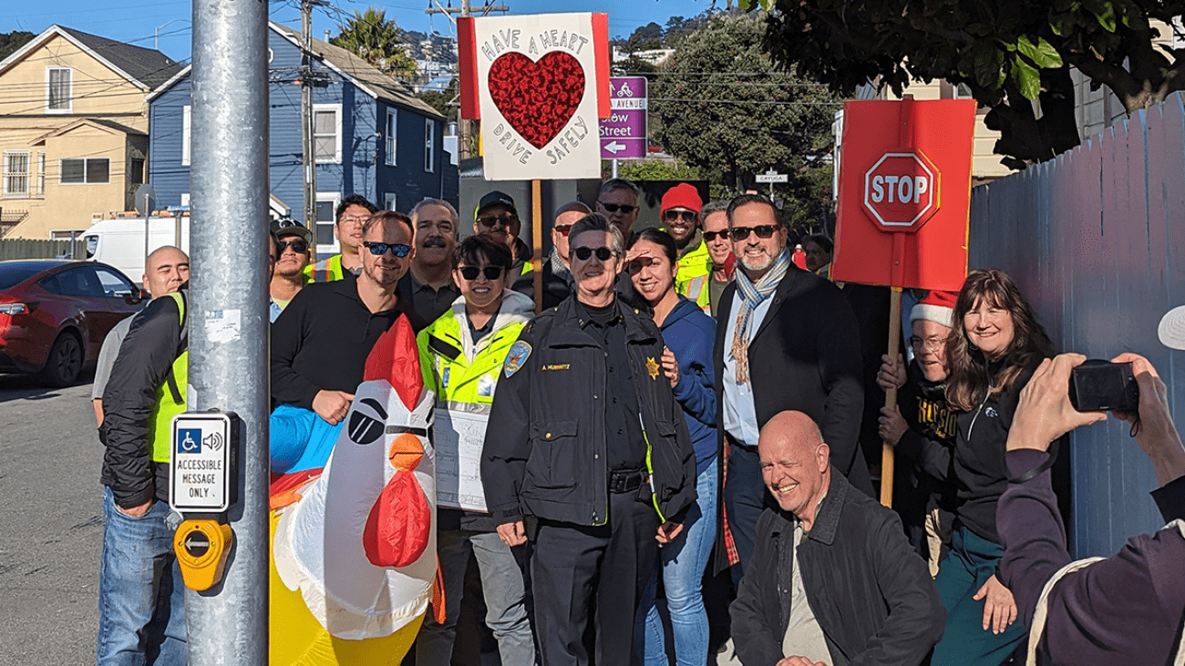 Staff from transit agencies, SF Public Works, SFPD, and community members standing by new traffic signal at Alemany and Rosseau