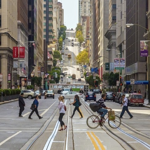 A photo of people walking and biking on Market Street, with a bus and cars in the background