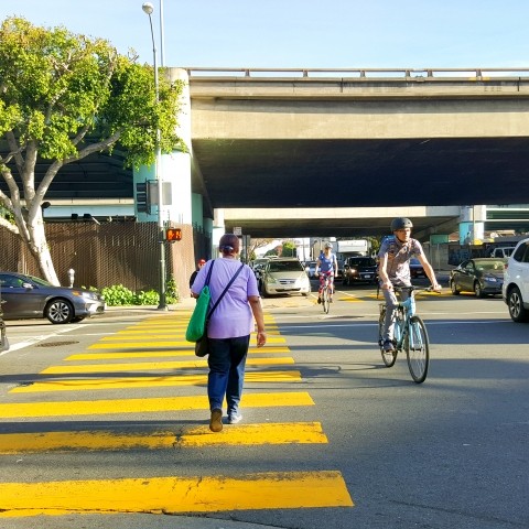 A freeway ramp intersection with cars, people walking, and people biking