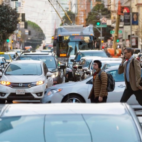 People cross crowded Mission Street as a bus waits in traffic