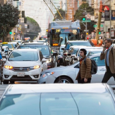 People cross crowded Mission Street as a bus waits in traffic