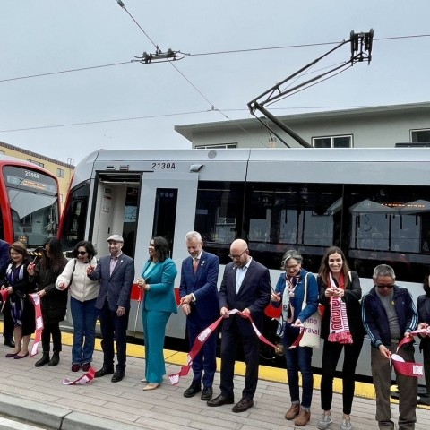 City officials, transportation officials and staff, and community members gathered in front of an L Taraval train to cut a ribbon